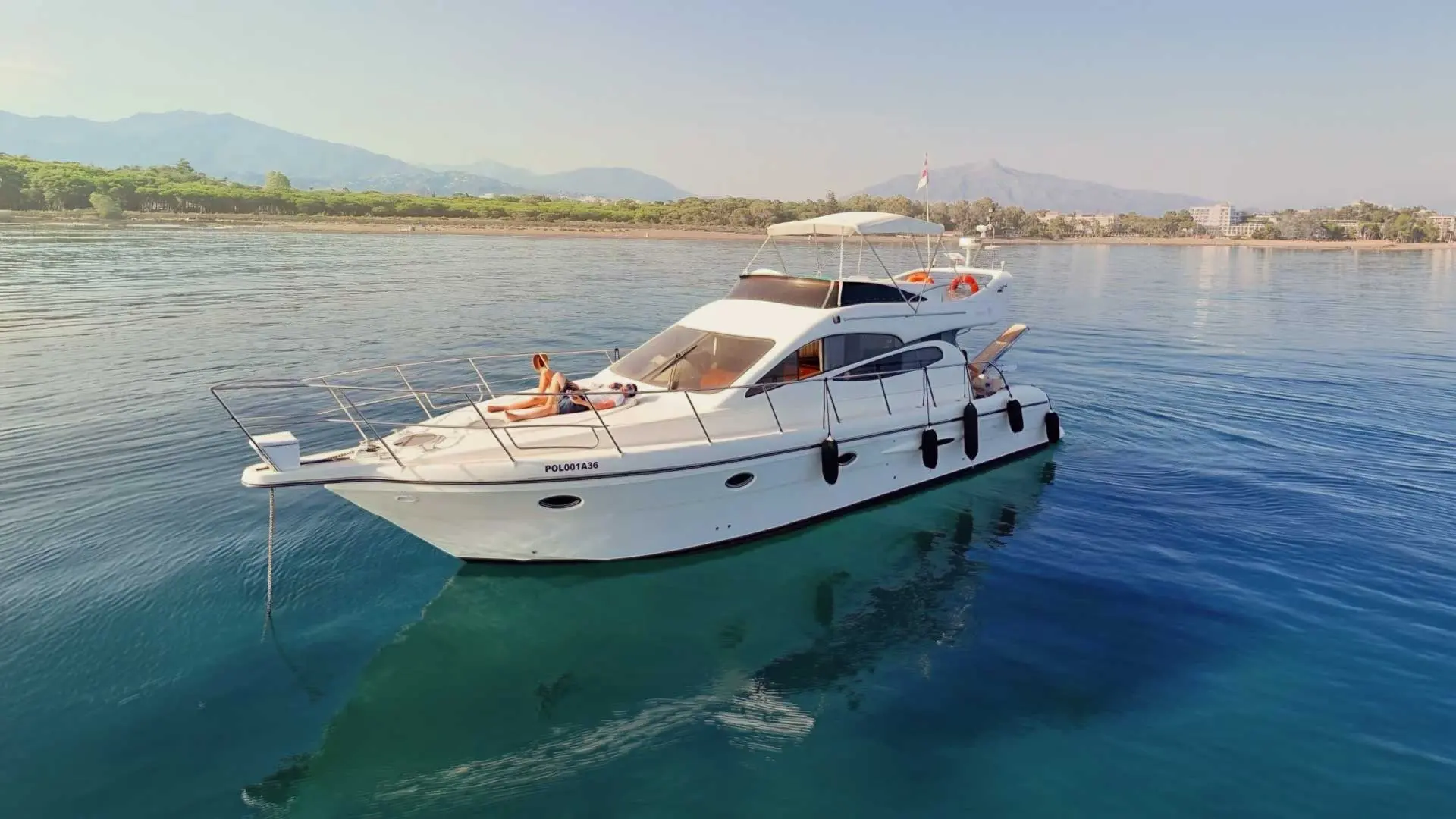 Yate blanca fondeada alquiles-de-bote-doqueve-majestic-46-en-marbella-y-fuengirola en aguas tranquilas junto a la costa, con montañas al fondo